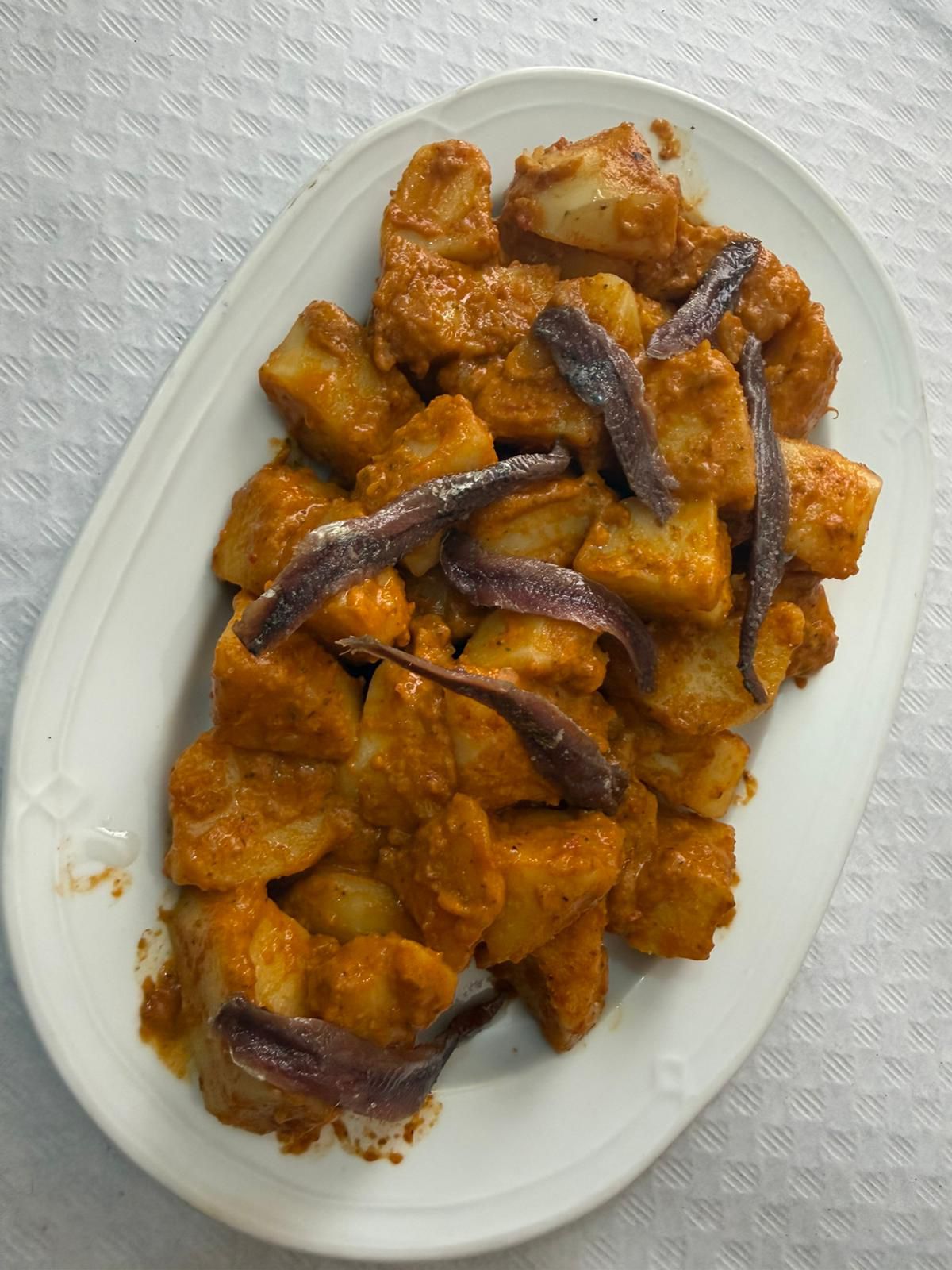Plato de yuca cocida acompañada de una salsa espesa de tomate y trozos de anchoa, servido en un plato blanco. Ideal para disfrutar como aperitivo o plato principal.