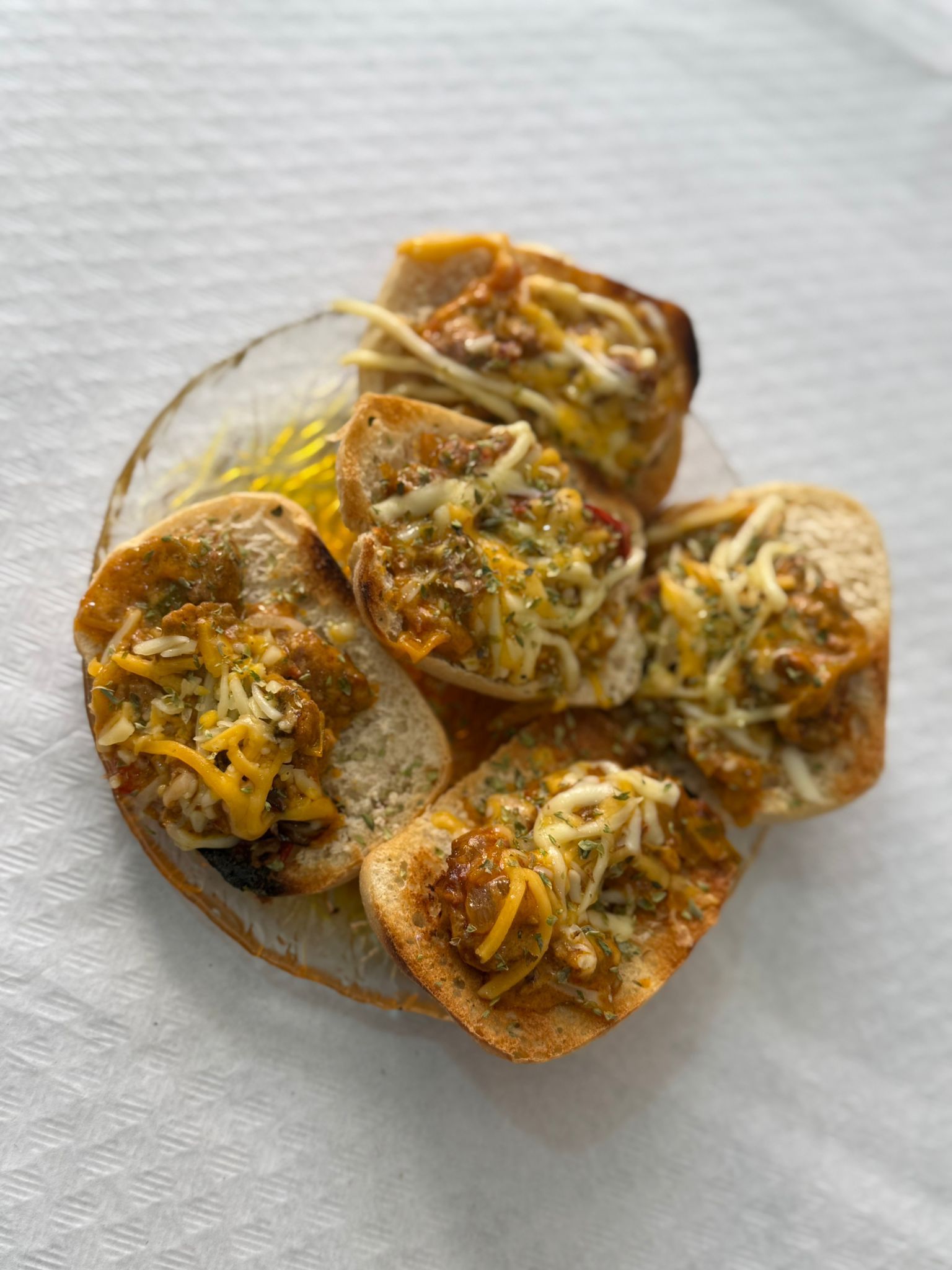 Plato de pan tostado con carne, salsa y quesos derretidos, decorado con hierbas frescas, sobre un fondo blanco. Ideal para un aperitivo delicioso.
