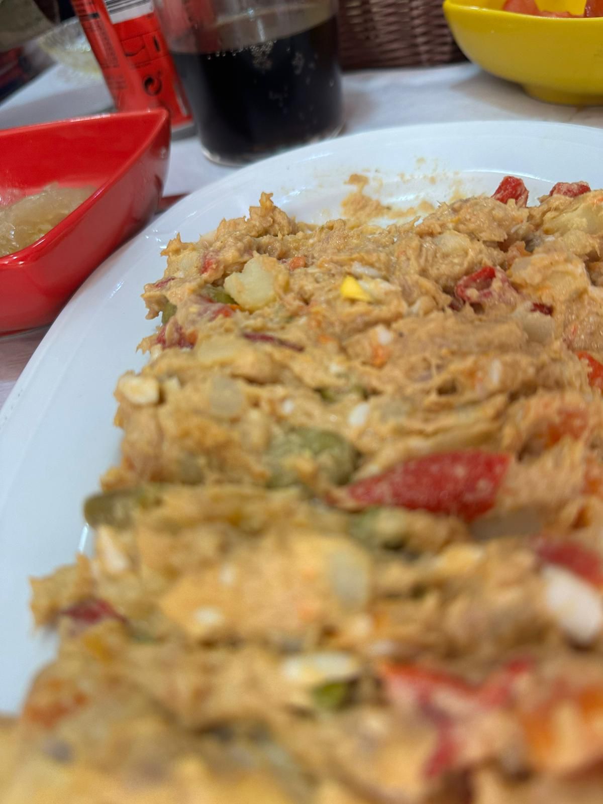 Plato de ensalada de atún con verduras, mostrando una textura cremosa y colorida, acompañado de un vaso de bebida oscura y un tazón de salsa.